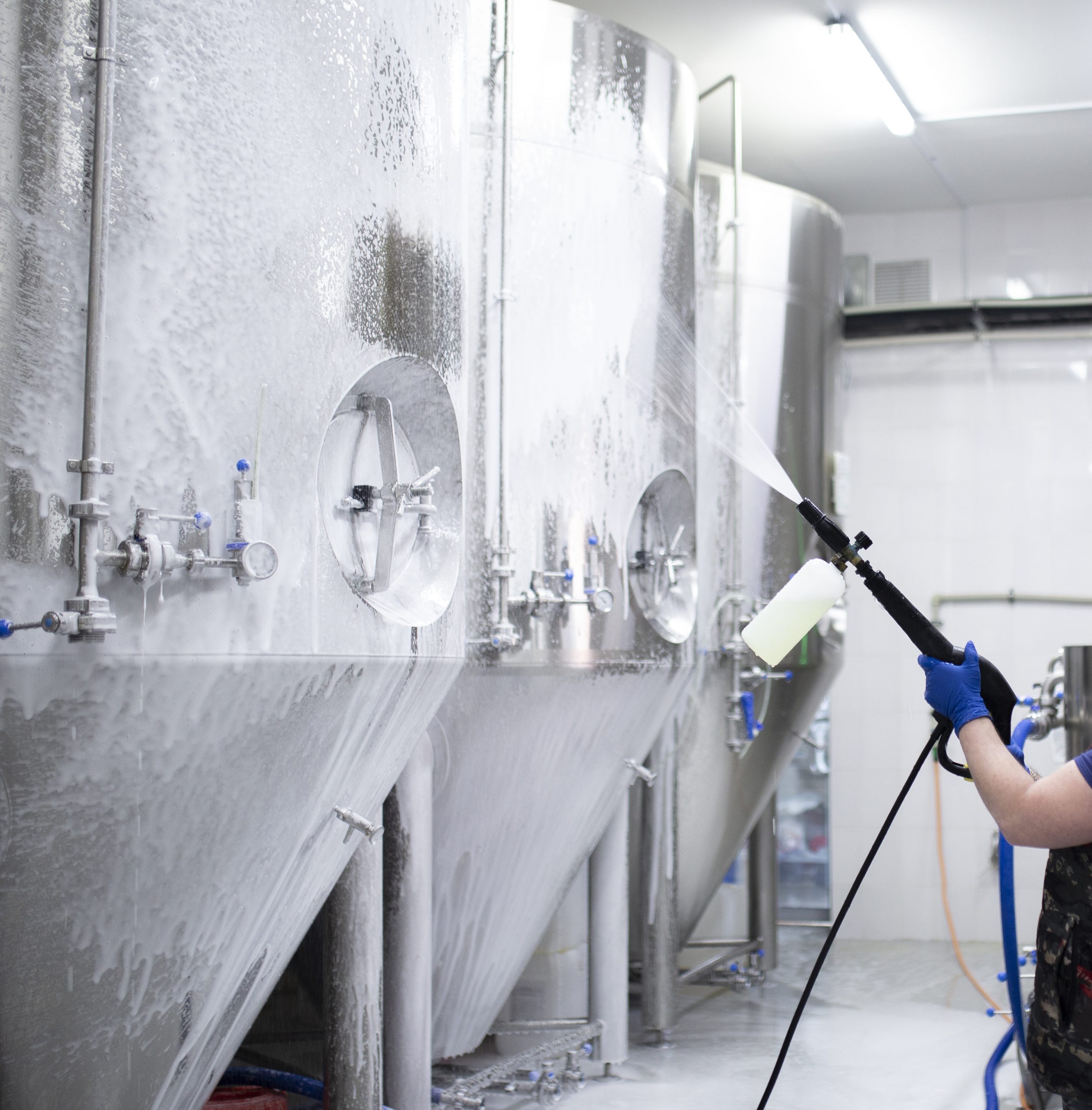 worker's hand hold a high pressure cleaner gun and put foam on equipment on the factory